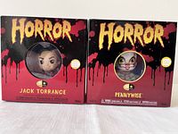 Two 5 Star Horror collectible figures - Jack Torrance and Pennywise, both in original red and black packaging with round windows showing stylized figure faces.