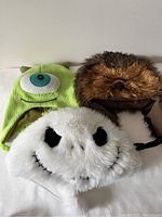 Three character winter hats grouped together: Mike Wazowski (green), Chewbacca (brown furry), and Jack Skellington (white plush).