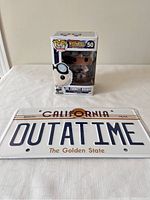 Front view showing Doc Brown Funko Pop in box and OUTATIME license plate side by side