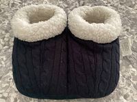 Photo showing the front view of the black slippers with white plush lining around the top edges, placed on a textured surface.