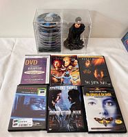 Top down view showing The Fifth Element, The Sixth Sense, Paranormal Activity, Demolition Man, The Silence of the Lambs DVDs and a Blockbuster DVD for Oceans Eleven, with a Neo bust figure and The Matrix discs in acrylic case in background.