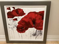 Frontal view of framed canvas art showing red flowers on gray and white background, with signature visible.