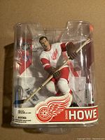 Front view of Gordie Howe action figure in packaging showcasing figure in red and white Detroit Red Wings uniform with hockey stick.
