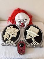 Front view of the Pennywise mask, female and male skull wall plaques, and the vintage-style red doorbell arranged on a white surface