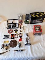 Overview of horror collectible lot with multiple small prop replicas, patches, bobblehead, Ghostbusters tin, Zombie cell phone holder, keychains