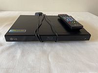 Front view of the black LG Blu-ray disc player showing USB port and Blu-ray logo with power cord on top.