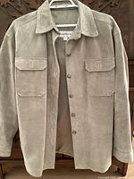 Front view of beige/tan Liz Claiborne suede leather jacket hanging on a hanger, showing button closure and flap pockets.