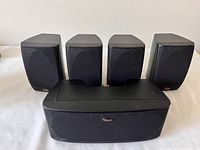 Five Polk Audio speakers arranged on table: Four small mountable speakers behind a larger center channel speaker.