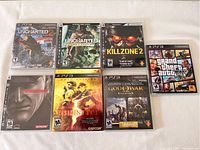 Photo of seven PlayStation 3 game cases arranged flat showing original cover art: Uncharted: Drake's Fortune, Uncharted 2: Among Thieves (sealed), Killzone 2, Metal Gear Solid 4: Guns of the Patriots, Resident Evil 5 Gold Edition, God of War Collection, and Grand Theft Auto V.