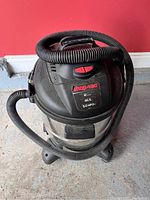 Shop-Vac stainless steel wet/dry vacuum with attached hose showing front and top with branding and power switch.