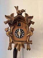 Front view of vintage German cuckoo clock showing detailed wooden carvings of birds and foliage, clock face with Roman numerals and cuckoo bird door.