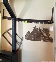 Long two-man crosscut saw hung horizontally on wall above wood stove pipe, showing the saw teeth and wooden handles.