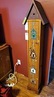 Full view of birdhouse-style cabinet against wall showcasing its height and front artwork with birdhouse motifs and vine accents.