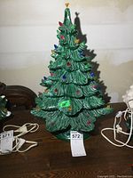 Full front view of the 20-inch tall ceramic Christmas tree showing green textured branches with multi-colored bulbs and a yellow bird topper. Power cord visible on the side.