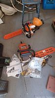 Overhead view of chainsaw body with orange bar cover, loose chain, manual in view