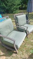 Two metal outdoor chairs with light green seat and back cushions, placed outside on grass.