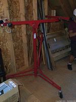 Full view of red metal drywall lift stand with tripod base and adjustable crossbar