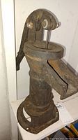 Full front view of the vintage cast iron hand pump mounted on a surface showing handle and spout with rust and wear.