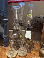 Five oil lamps arranged on wooden surface: three larger at back, two smaller at front