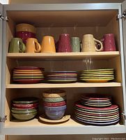 Three-shelf cabinet loaded with mugs on top, medium and large plates on middle, bowls and smaller plates on bottom