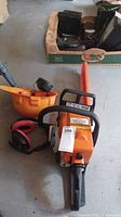 Stihl chainsaw with attached guide bar and chain alongside hardhat and ear protection