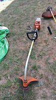 Full view of gas string trimmer laying on grass, showing length and D handle on shaft.