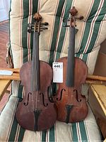 Overview of two unbranded violins resting on striped cushion