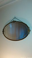 Full view of the antique oval mirror hanging on a wall, showing the brass frame and reflective surface with a beveled edge.