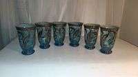 Front view of six blue glass tumblers with silver overlay floral and leaf designs arranged in a row.