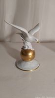 Porcelain bird figurine, left side view showing bird perched on gold sphere on a circular white base with gold trim.