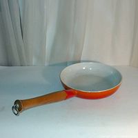 Side view of vintage large orange cast iron skillet with wooden handle showing interior and exterior enamel finishes.