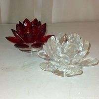 Pair of crystal lotus flower candleholders on a white surface. One red and one clear, both with faceted petal design.
