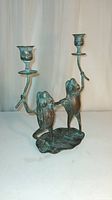 Frontal view of two bronze frogs dancing and holding two candle holders on a lily pad base, showing the full sculpture from the front.
