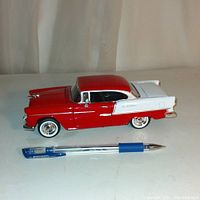 Side profile of red and white Chevy Bel Air die cast toy car with blue pen for scale