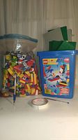 Photo showing large zip-top bag filled with assorted LEGO pieces, blue LEGO pail with LEGO System 1708 box on front, pen, and tape for scale