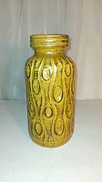 Front angle view of the yellow West Germany pottery vase showing the circular and wavy raised decorative pattern and neck detail.