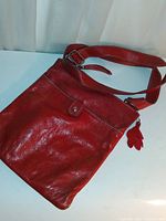 Front view of the red leather messenger bag showing adjustable strap and front snap pocket with leather leaf zipper pull charm.