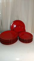 Full set of 16 red flame plates grouped by size, dinner plates stacked on left, lunch plates stacked on right, against a white backdrop.