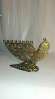 Brass menorah candleholder shaped like a bird with floral vine cutout patterns, viewed from the front angle showing nine candle holders.