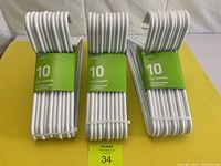 Three unopened packs of white plastic coat hangers stacked upright, displaying the full lot.