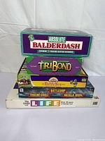 Stack of five board game boxes including Absolute Balderdash, TriBond, Cranium Family Fun, Battleship (non-electronic), and Life.