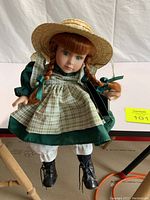 Front view of porcelain Anne of Green Gables doll in green dress, apron, stockings, boots, and straw hat.