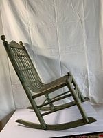 Side view of child's antique bentwood rocking chair showing slatted seat and backrest, green paint finish, and curved rockers.