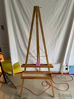Front view of the full wooden artist's easel against a white backdrop, showing tripod legs, chain stabilizer, and movable canvas tray.