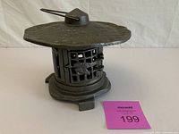 Front view of the black cast iron garden lantern showing textured flat top, lattice sides with bird design, and three small feet.