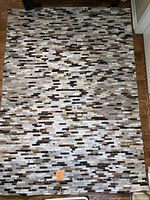 Full view of the cowhide patchwork rug spread out on a wood floor. Shows the multicolored rectangular patches in a horizontal arrangement.