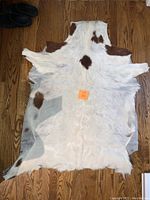 Full view of cream and brown cowhide rug on wood floor with sticker 223 on top