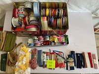 Top-down view of large assortment of ribbon spools neatly arranged with two metal storage tins and several loose packs on white surface.