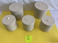 Five beige leatherette round storage bins with lids, arranged in two rows on a yellow surface, showing two larger and three smaller bins.