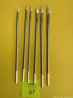 Six silver-handled Silverwhite 1501 flat paint brushes with white tips arranged on a yellow background.